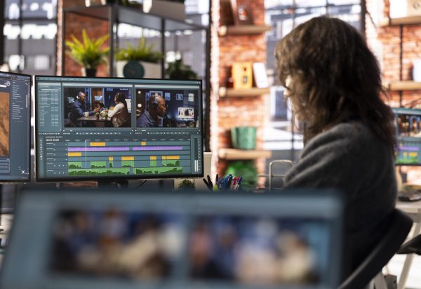 Female filmmaker working on media post production from agency office, ensuring the editing timeline and color correction for a video shoot. Tech driven workspace showcases a digital workflow.