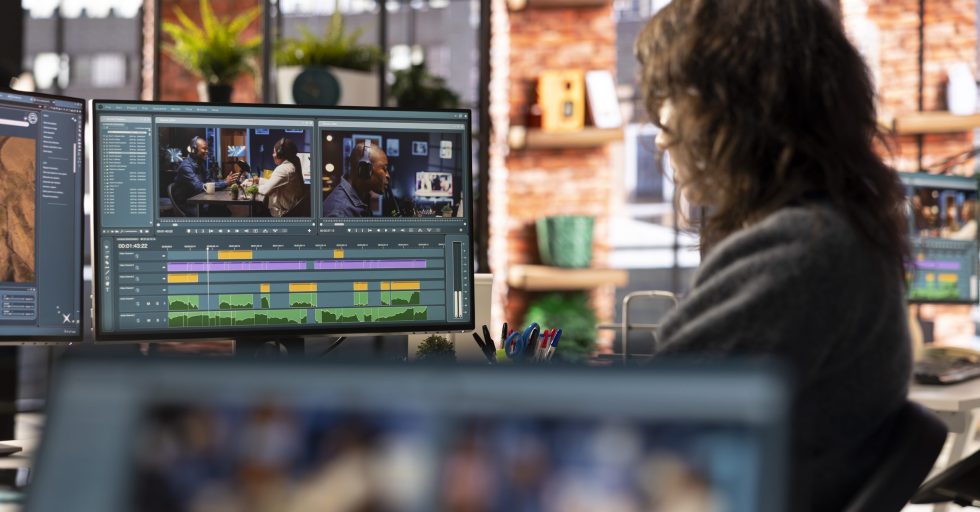 Female filmmaker working on media post production from agency office, ensuring the editing timeline and color correction for a video shoot. Tech driven workspace showcases a digital workflow.